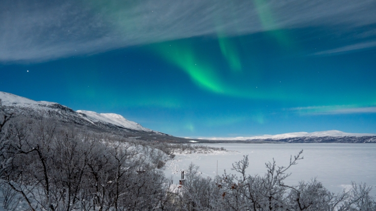 Green auroras dancing over a lake in Abisko, Sweden