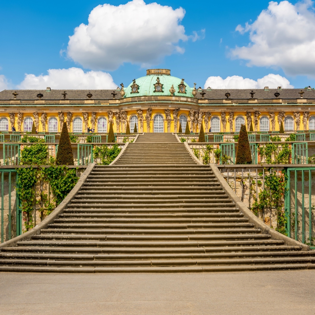 A grand outdoor staircase leads up to the yellow, ornate Sanssouci Palace